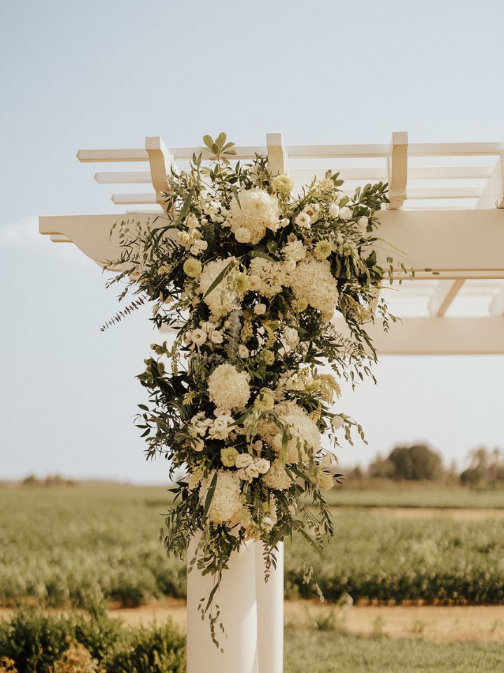 Closeup of flower arrangement in white and green on a wedding ceremony pergola.