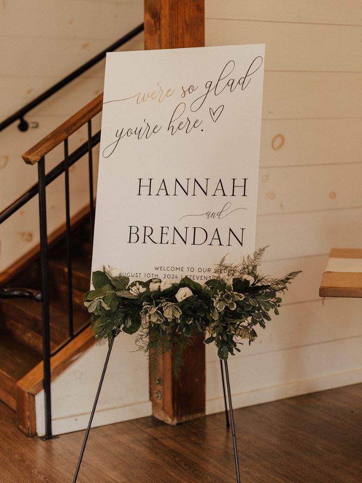 Welcome sign for wedding on an easel with greenery at base.