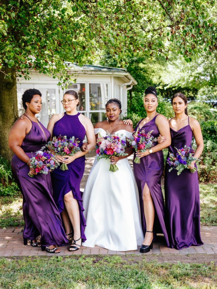 Bride and bridesmaids pose with bouquets for a summer purple wedding.