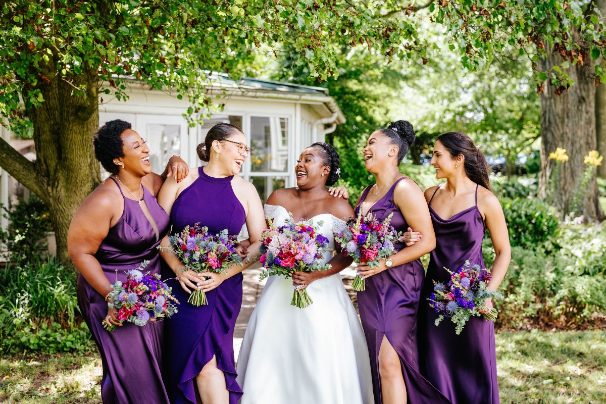Bride and bridesmaids in purple dresses in a line with their jewel tone bouquets.