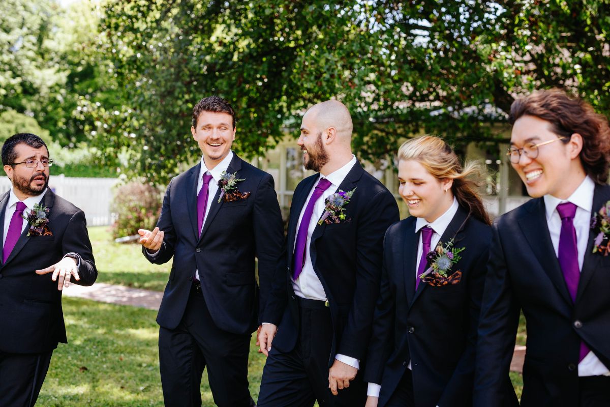 Groom and groomsmen party walk in black suits.