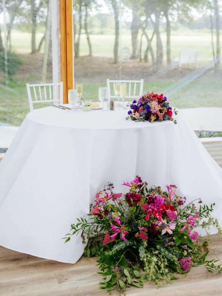 Sweetheart table has large flower arrangement from ceremony at the base, and bouquet sitting on the top.