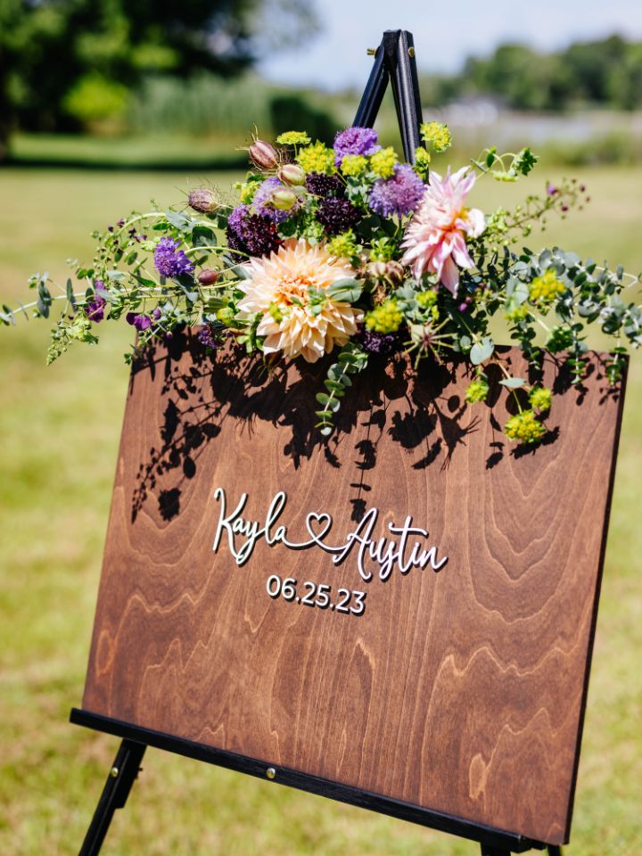 Welcome sign with flowers and greenery on top edge.