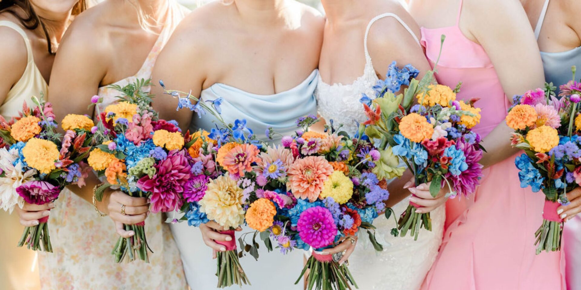 Closeup of bridesmaids in pastel dresses holding rainbow color flowers.