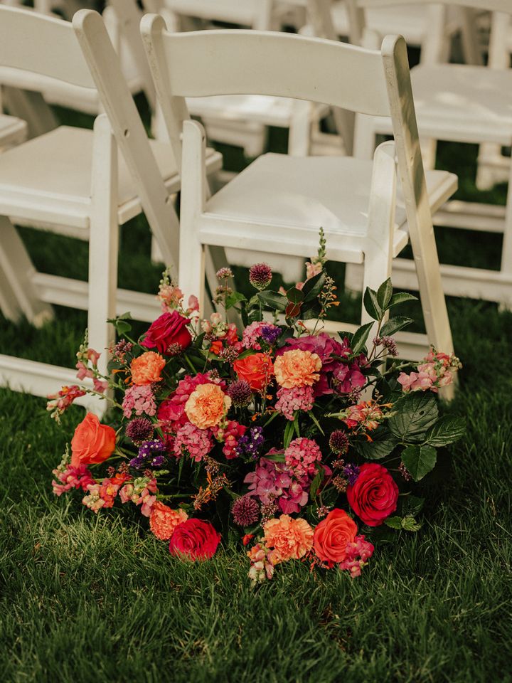 Flower arrangement sits at base of chair at entrance to outdoor wedding ceremony aisle.