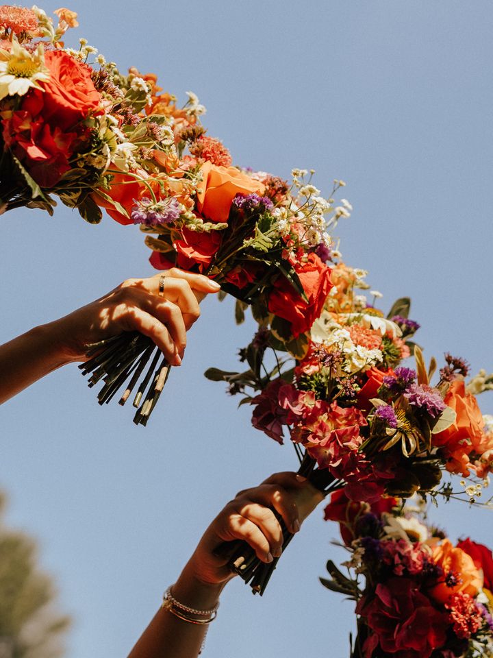 Bridesmaids hold up bouquets to blue sky.