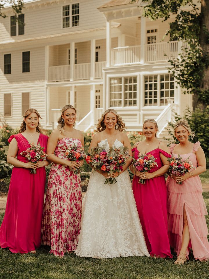 Bridesmaids in pink patterned dresses line up with bride, holding their flower bouquets.