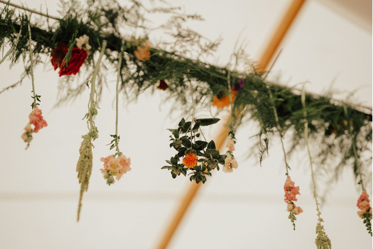 Closeup of hanging greenery and flower installation on tent lighting.