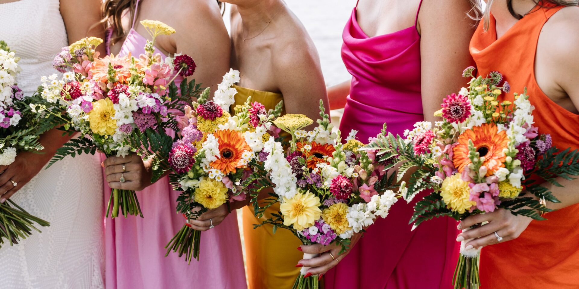 Closeup of bridesmaid bouquets, with colorful pink, yellow, and orange flowers and dresses.