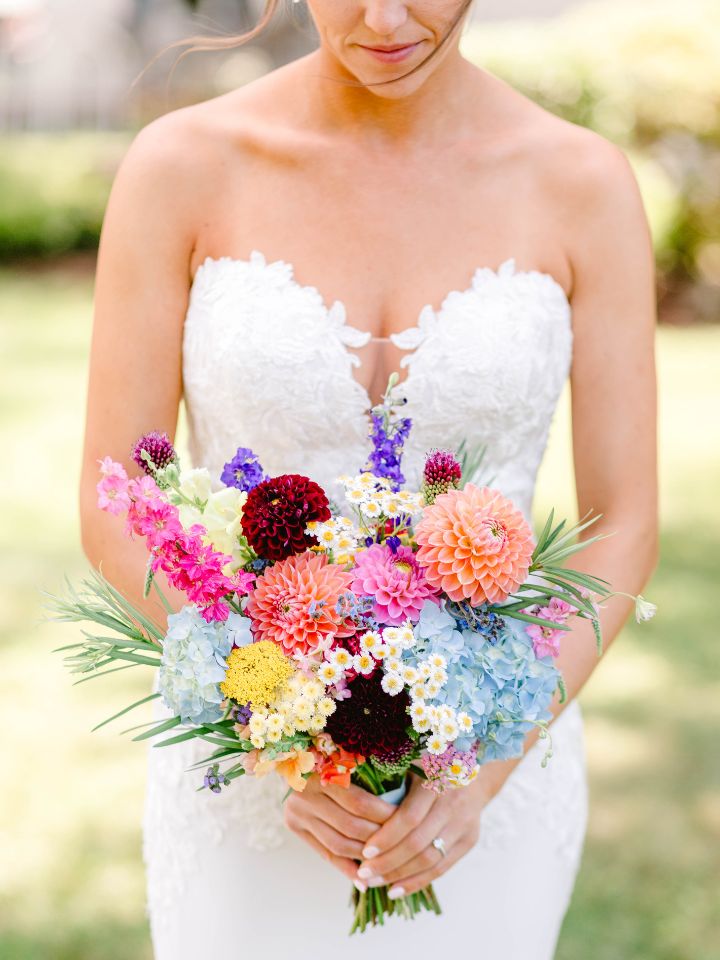 Bride holds her colorful summer wedding flowers bouquet.