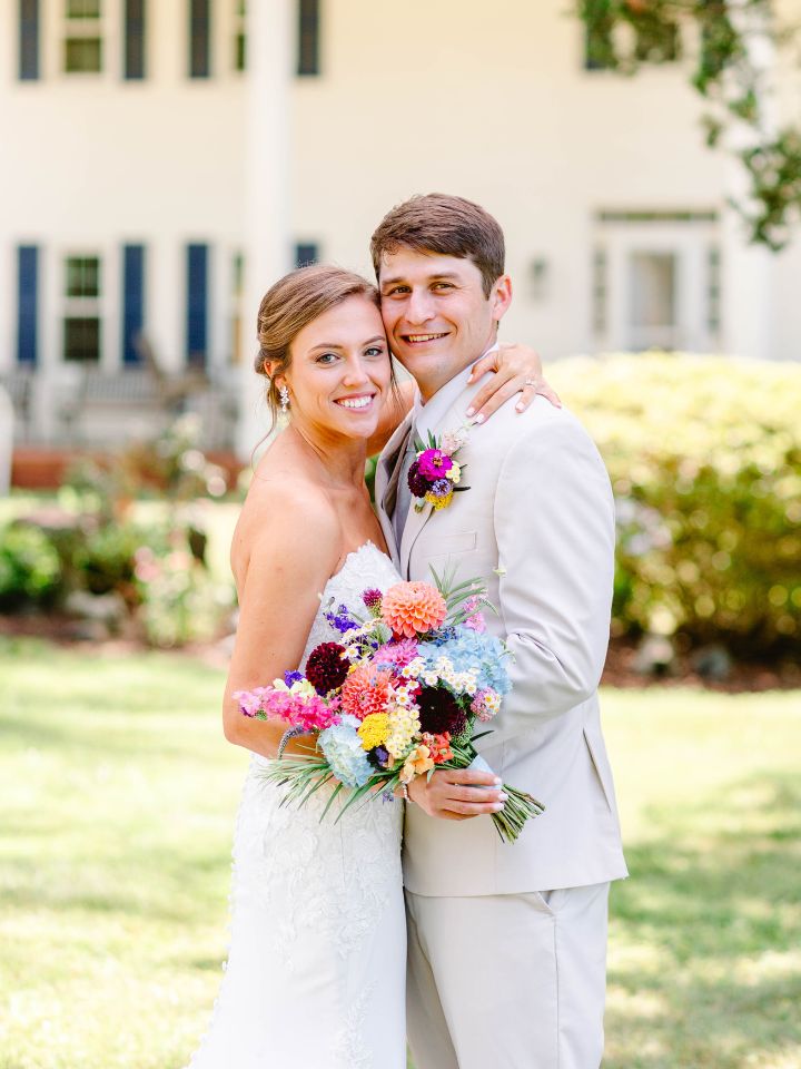 Bride and groom pose in front of old home with large porch.