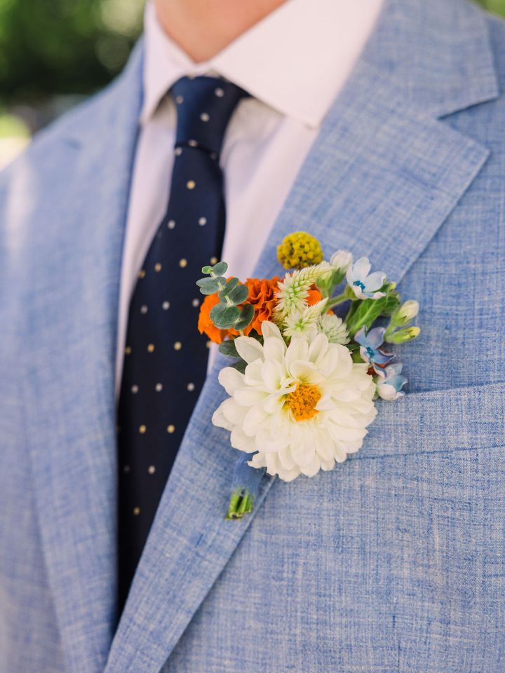 Closeup of pin on boutonniere on a light blue suit with navy blue tie.