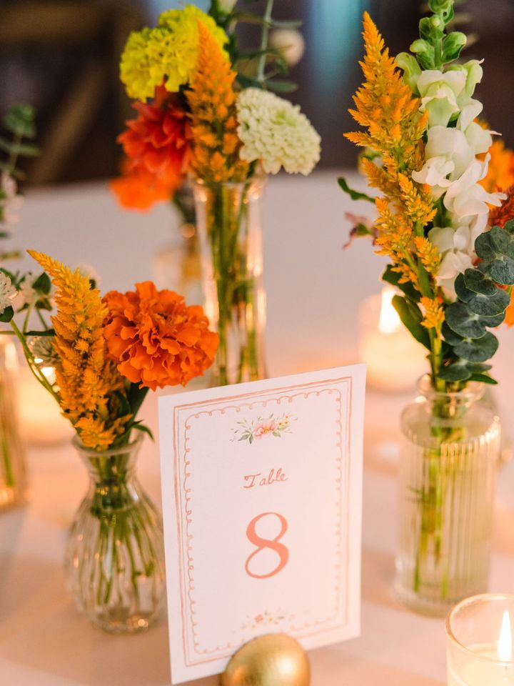 Orange, blue, white, and yellow flowers in bud vases next to votive candles.