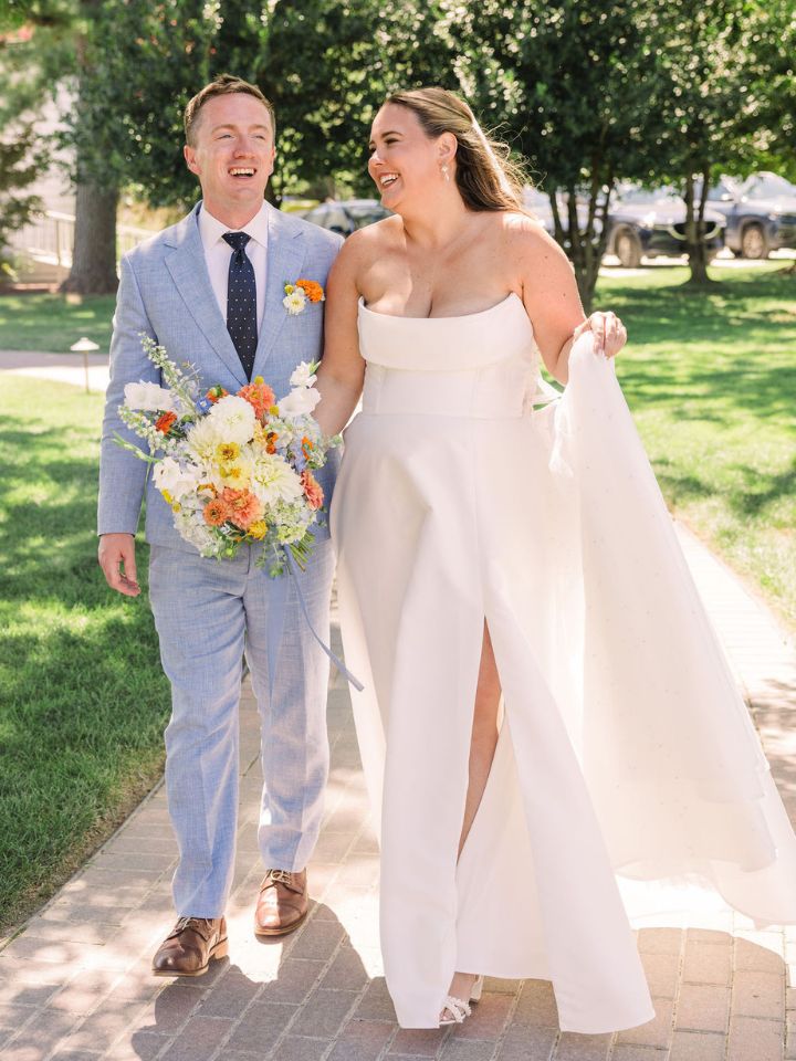 Bride and groom walk towards camera while holding flower bouquet.
