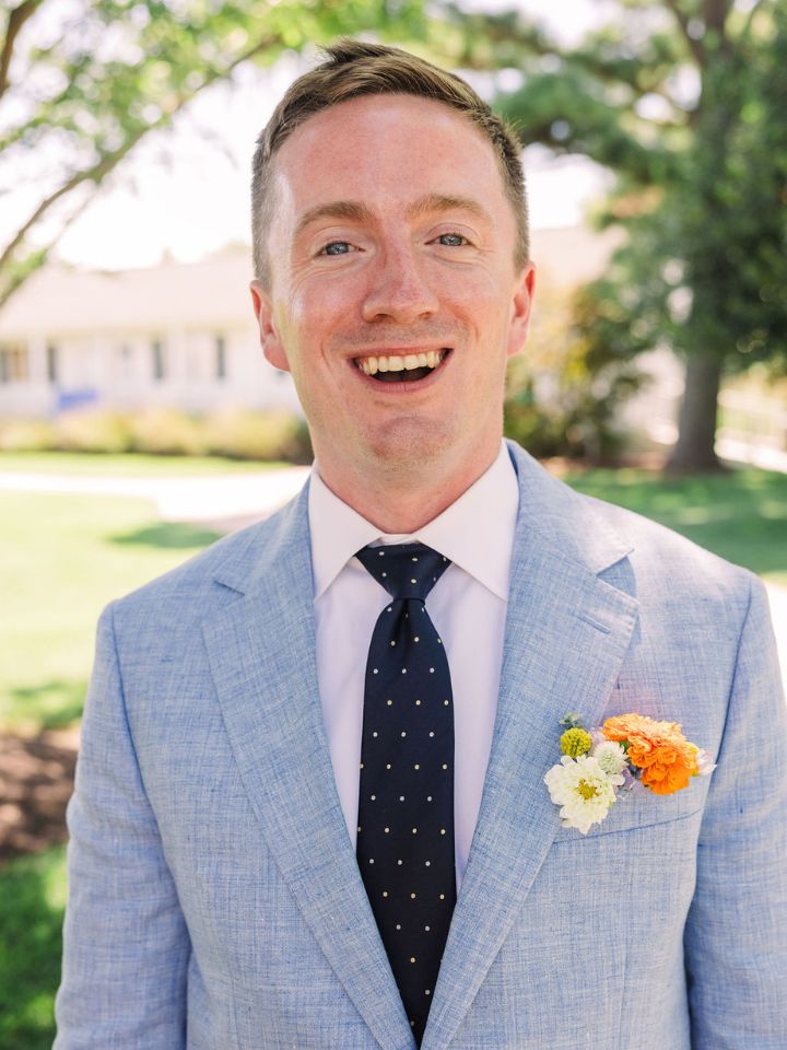 Groom smiles at camera, with orange and white flower pocket square.