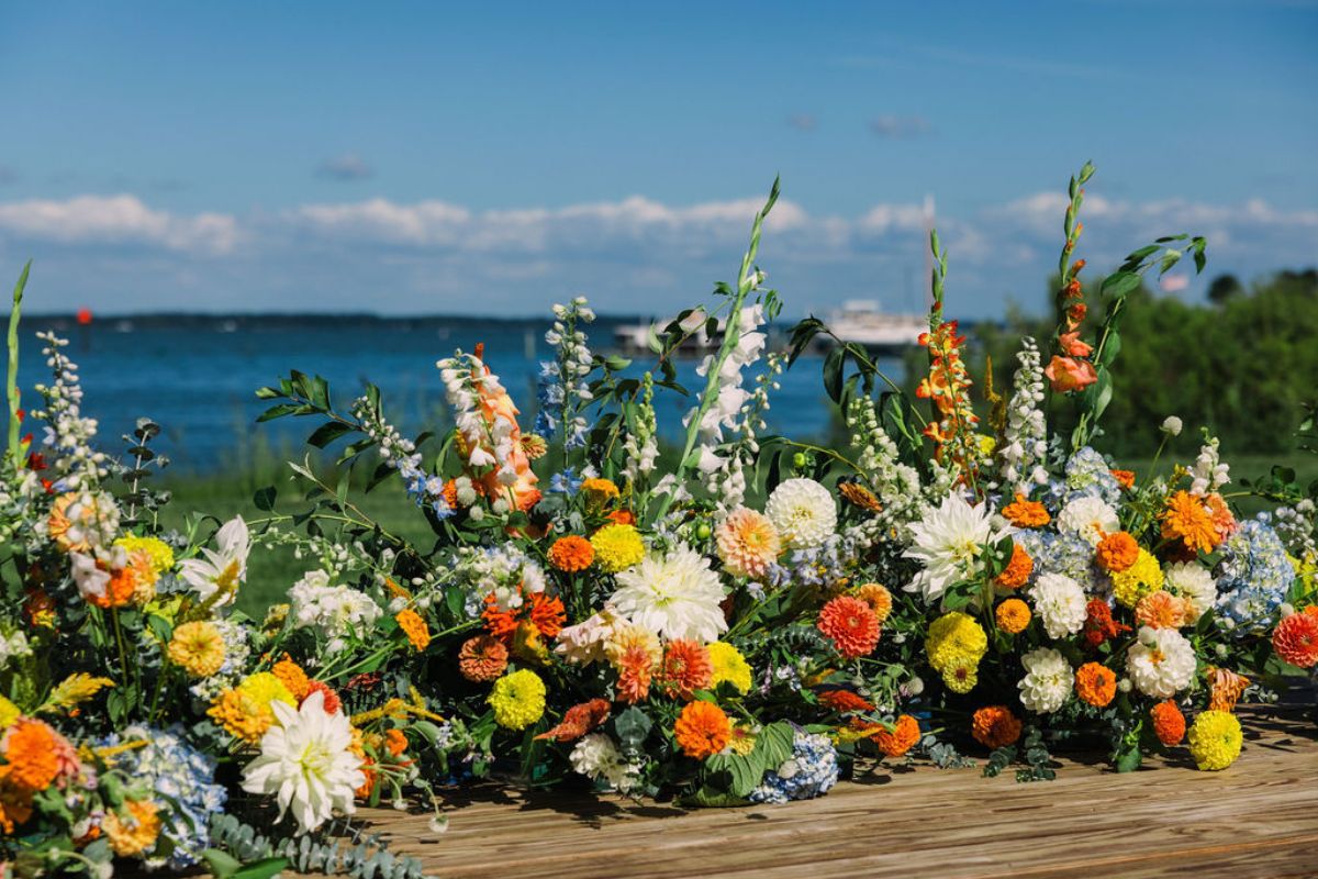 Large flower arrangements in blue, white, orange, and yellow for a wedding ceremony.