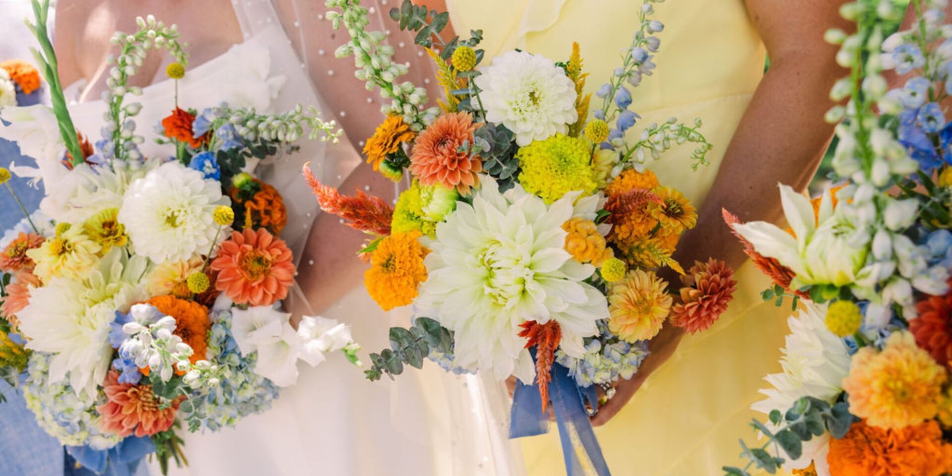 Closeup of bridal and bridesmaid bouquets in blue, white, orange, and yellow.
