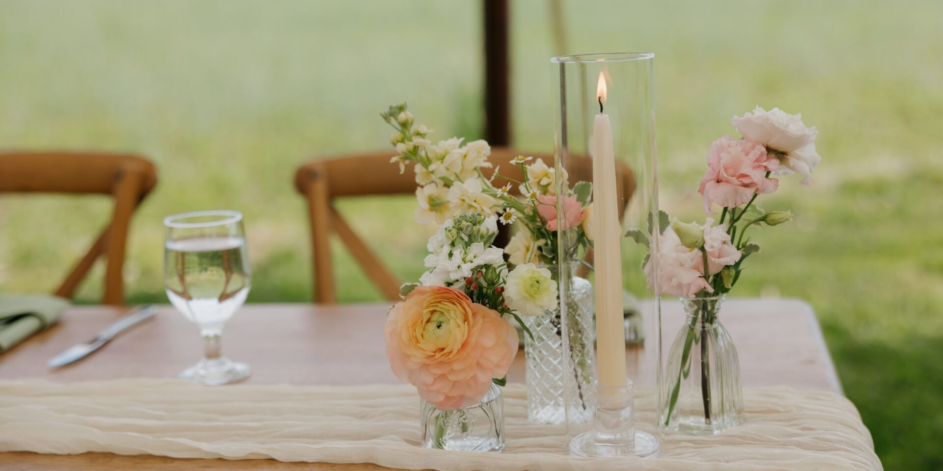 Flower bud vases in pastel peach on a sweetheart table with a taper candle.