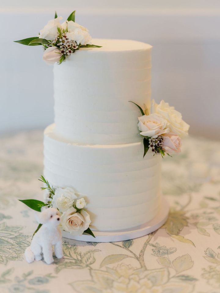 White two tier wedding cake with small flower accent and mini dog figurine.