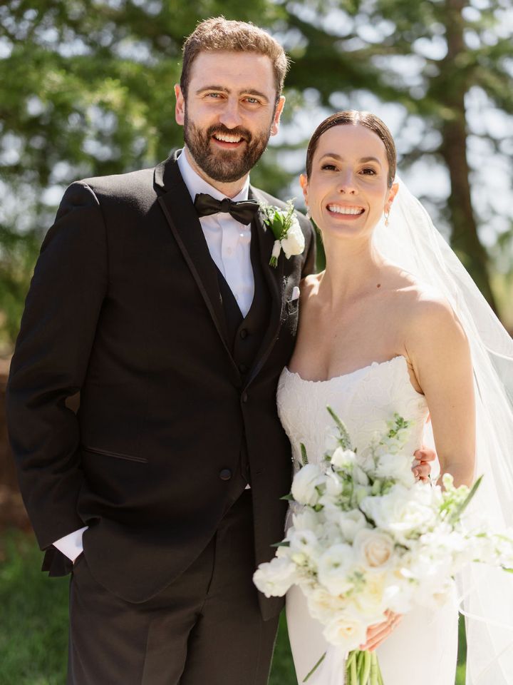 Bride and groom pose for camera holding her bouquet.