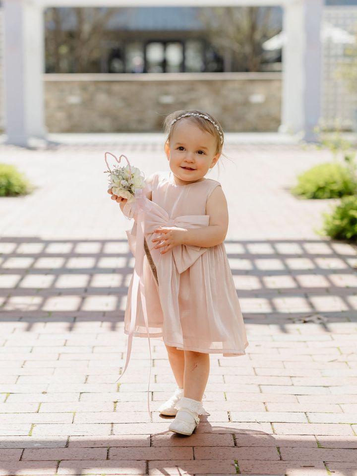Toddler girl in pale pink dress holds a flower wand.
