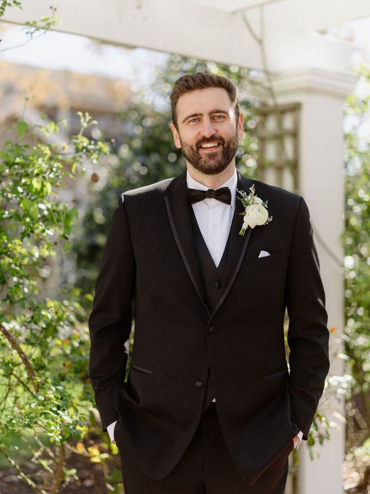 Groom in black tuxedo with white flower boutonniere.