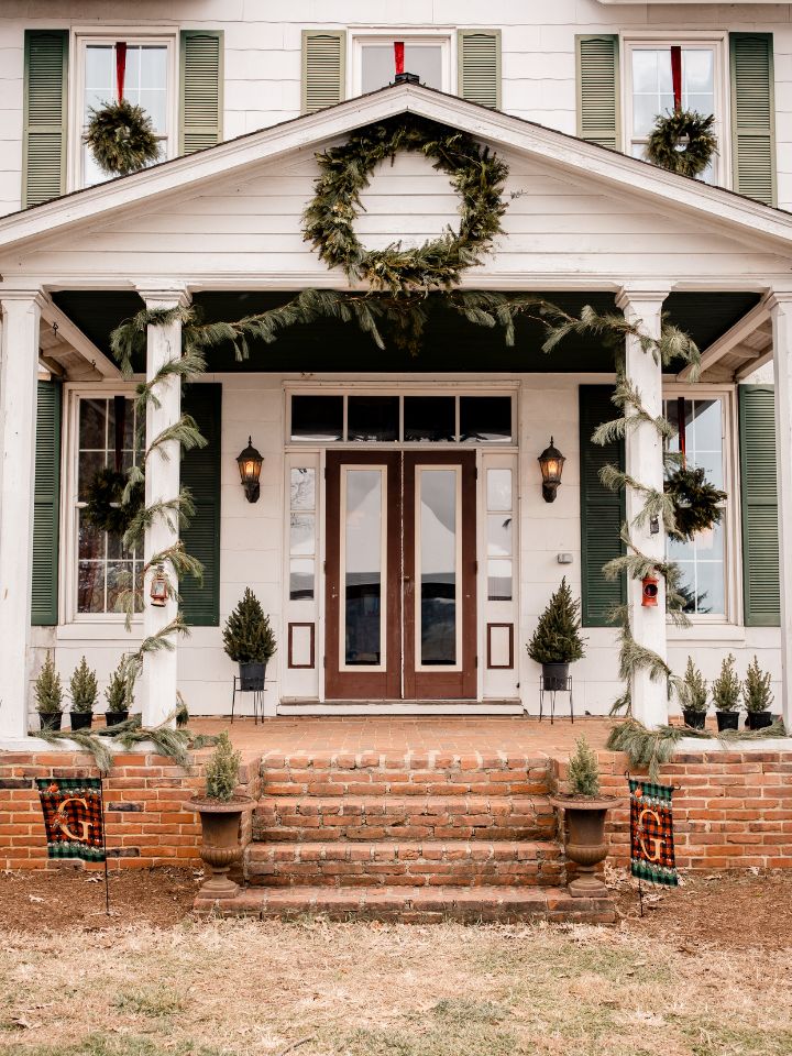 Front porch of old house decorated with evergreen garlands and wreaths.