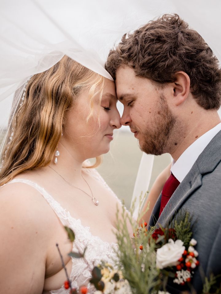 Bride and groom pose under veil.