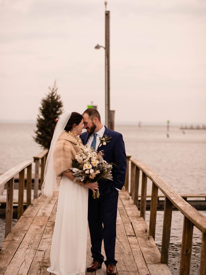 Bride and groom pose on dock.