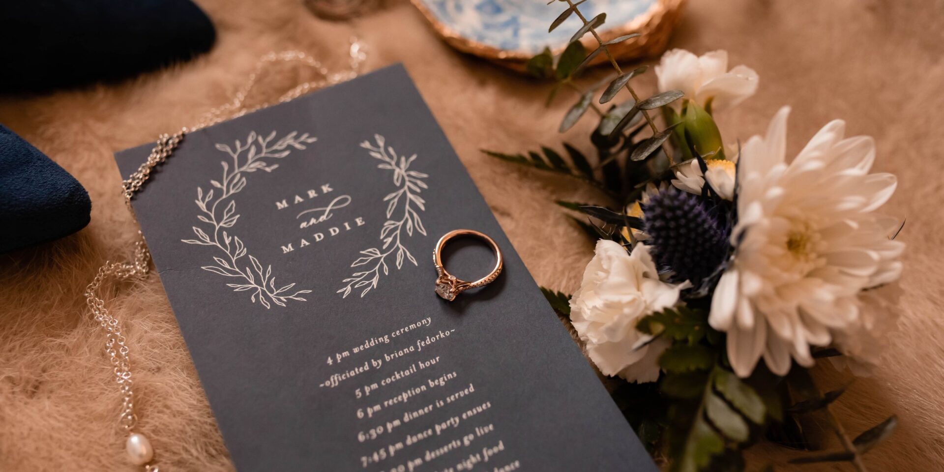 Closeup of wedding invitation, rings, and flowers
