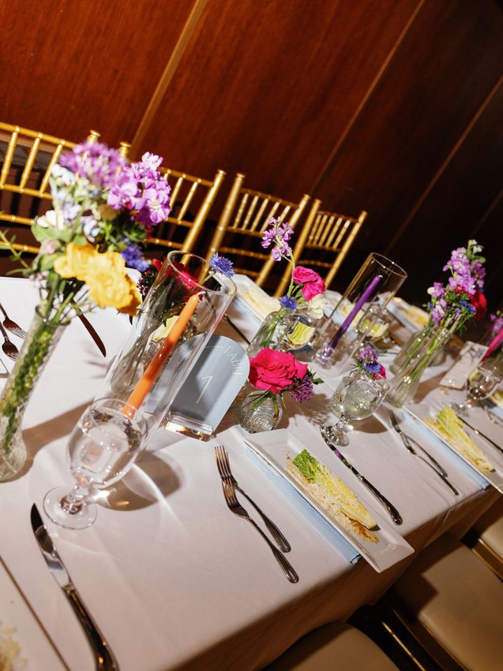 Long rectangular guest table at wedding reception with flower bud vases.