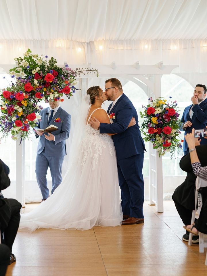Bride and groom kiss under wedding ceremony arch.
