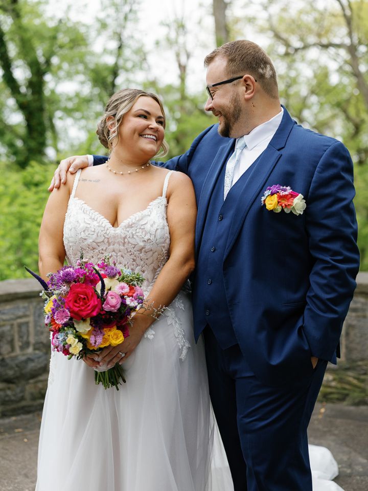 Bride and groom smile at each other, holding bouquet.