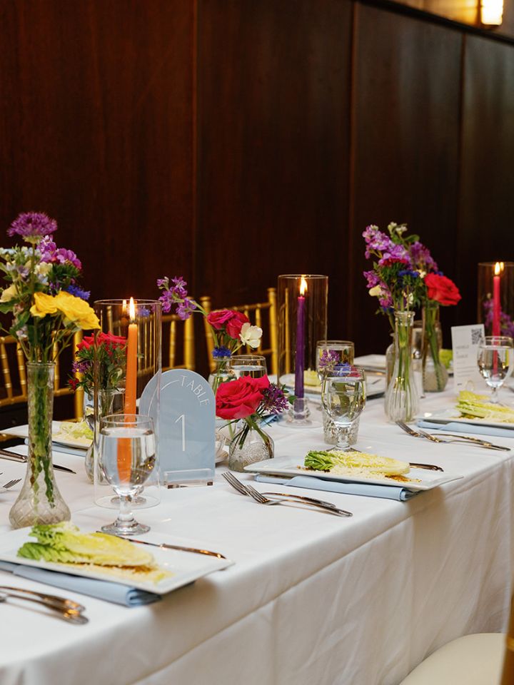 Bright flower bud vases and taper candles as rectangular table centerpiece at wedding reception.