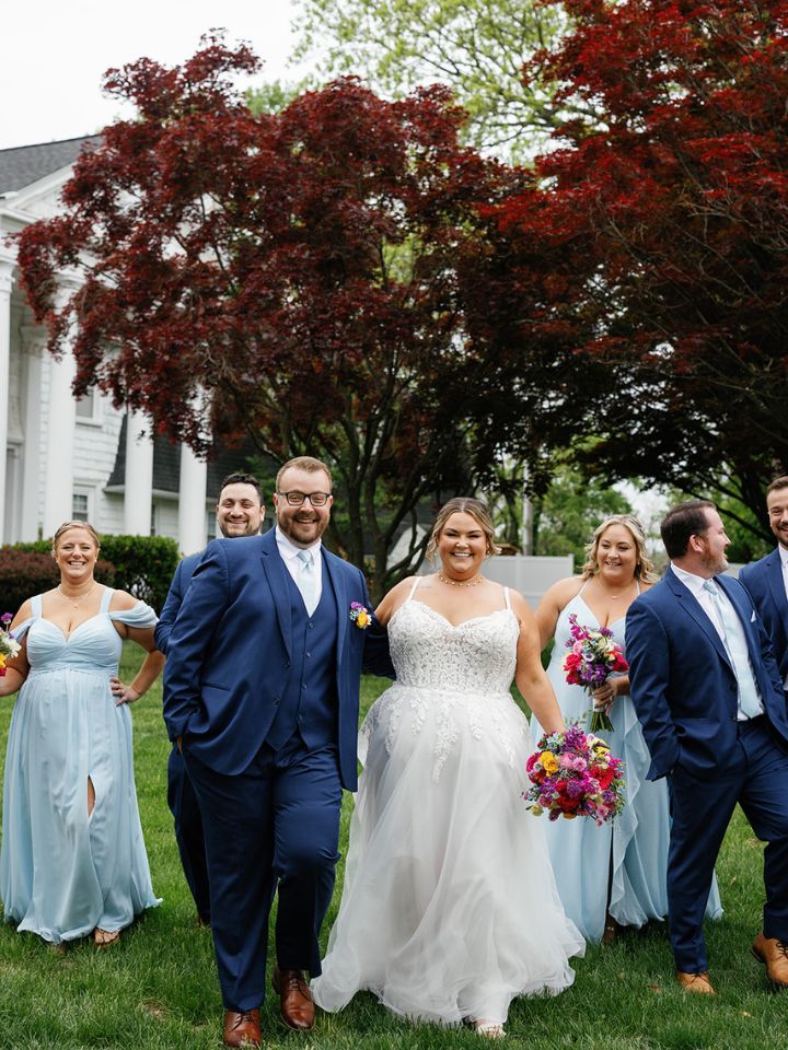 Bride and groom walk with wedding party across lawn.