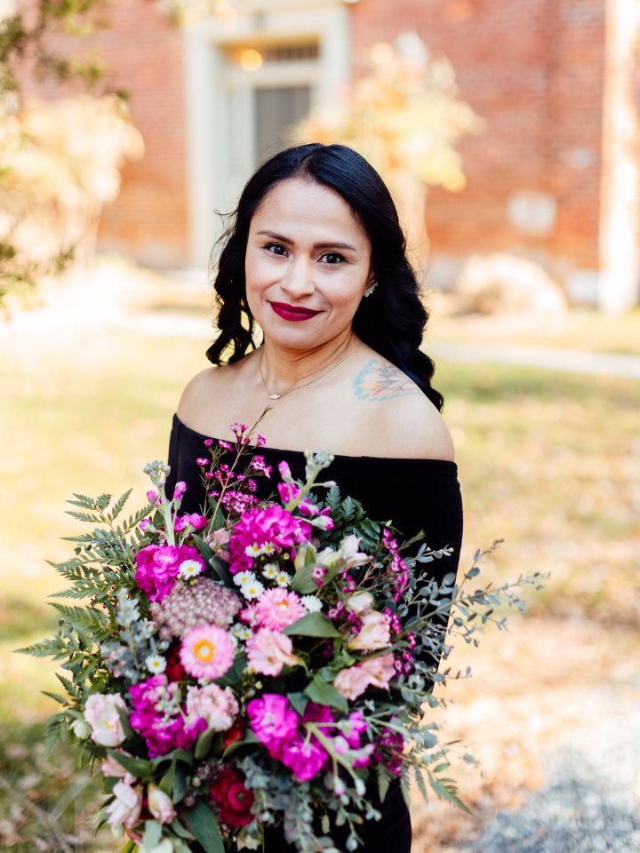 Bride in black dress holds colorful jewel tone winter bouquet.