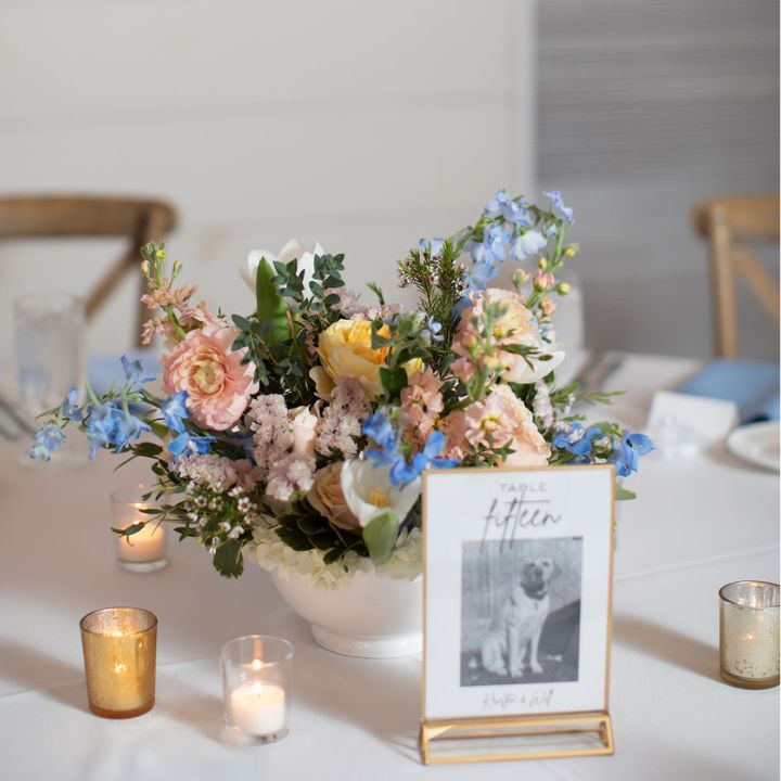White ceramic compote dish with pastel flower arrangement as a wedding guest table centerpiece.