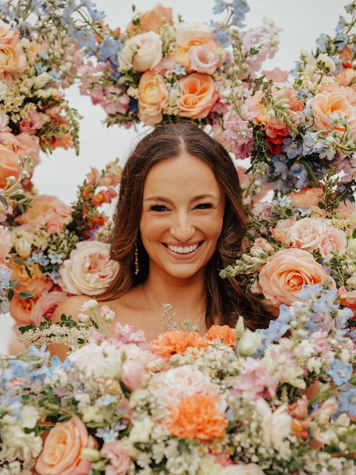 Bride smiles inside of a frame of flower bouquets.