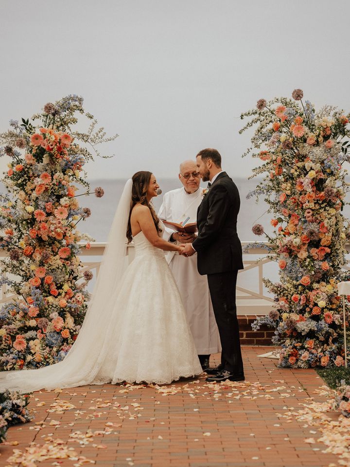 Bride and groom exchange vows between two large flower column arrangements.