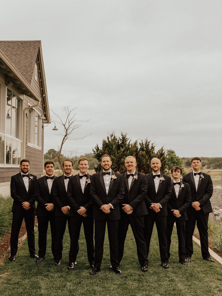 Groom and groomsmen in black tuxedos with pin-on flower boutonnieres.