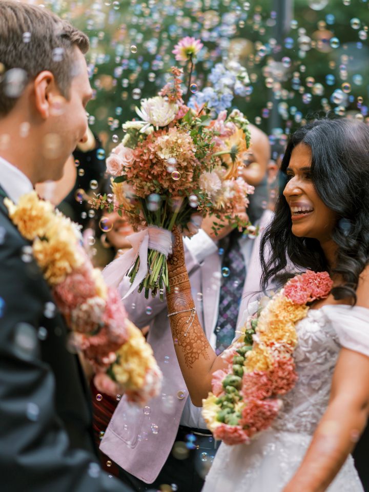 Bride and groom wear peach, pink, orange toned flower jai malas.