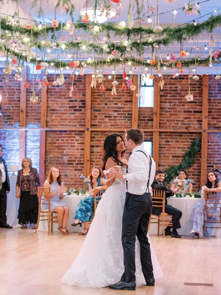 Couple dances under lights, greenery, and suspended flowers at the AVAM.