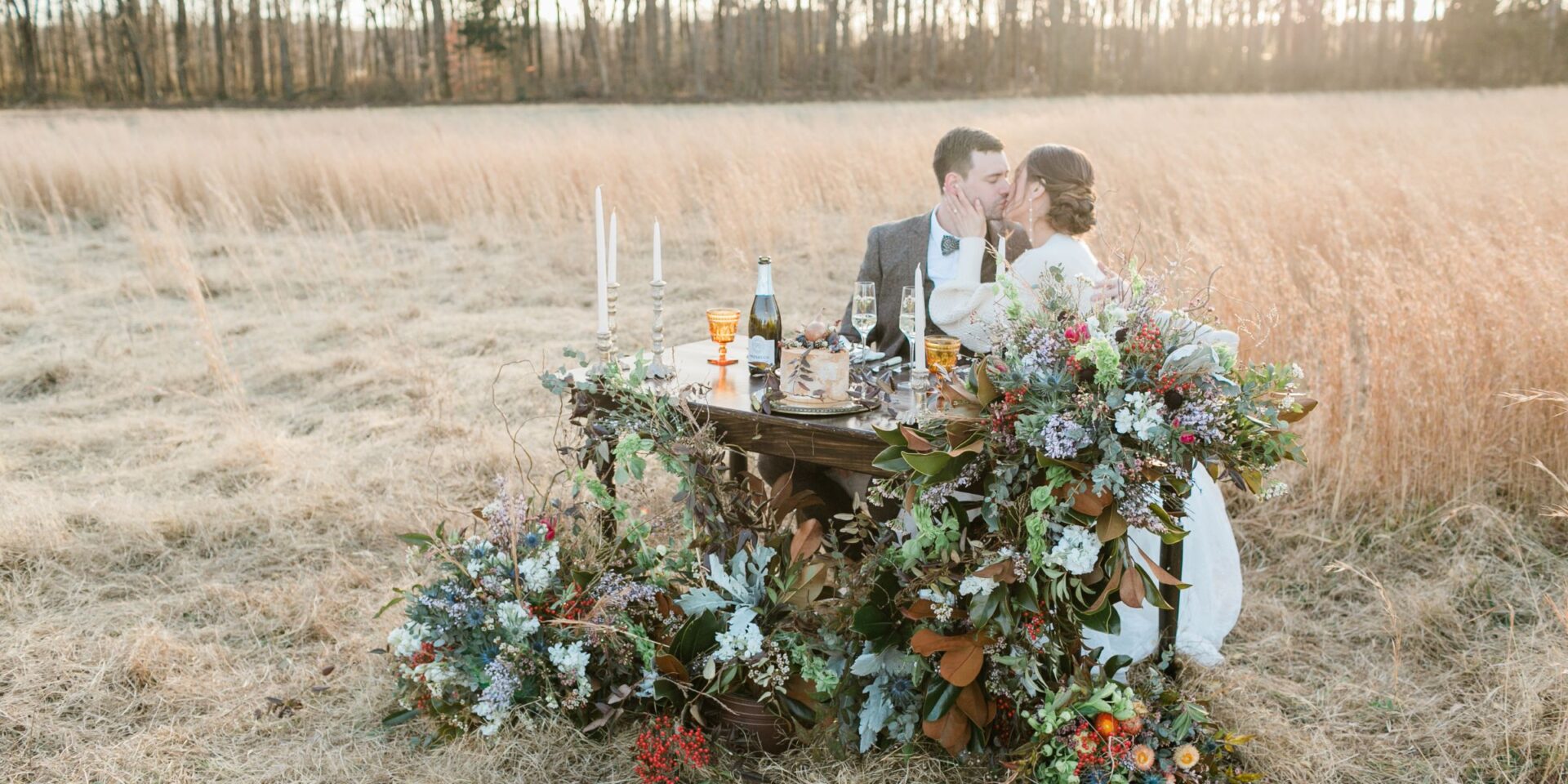 Couple kisses at sweetheart table in field.